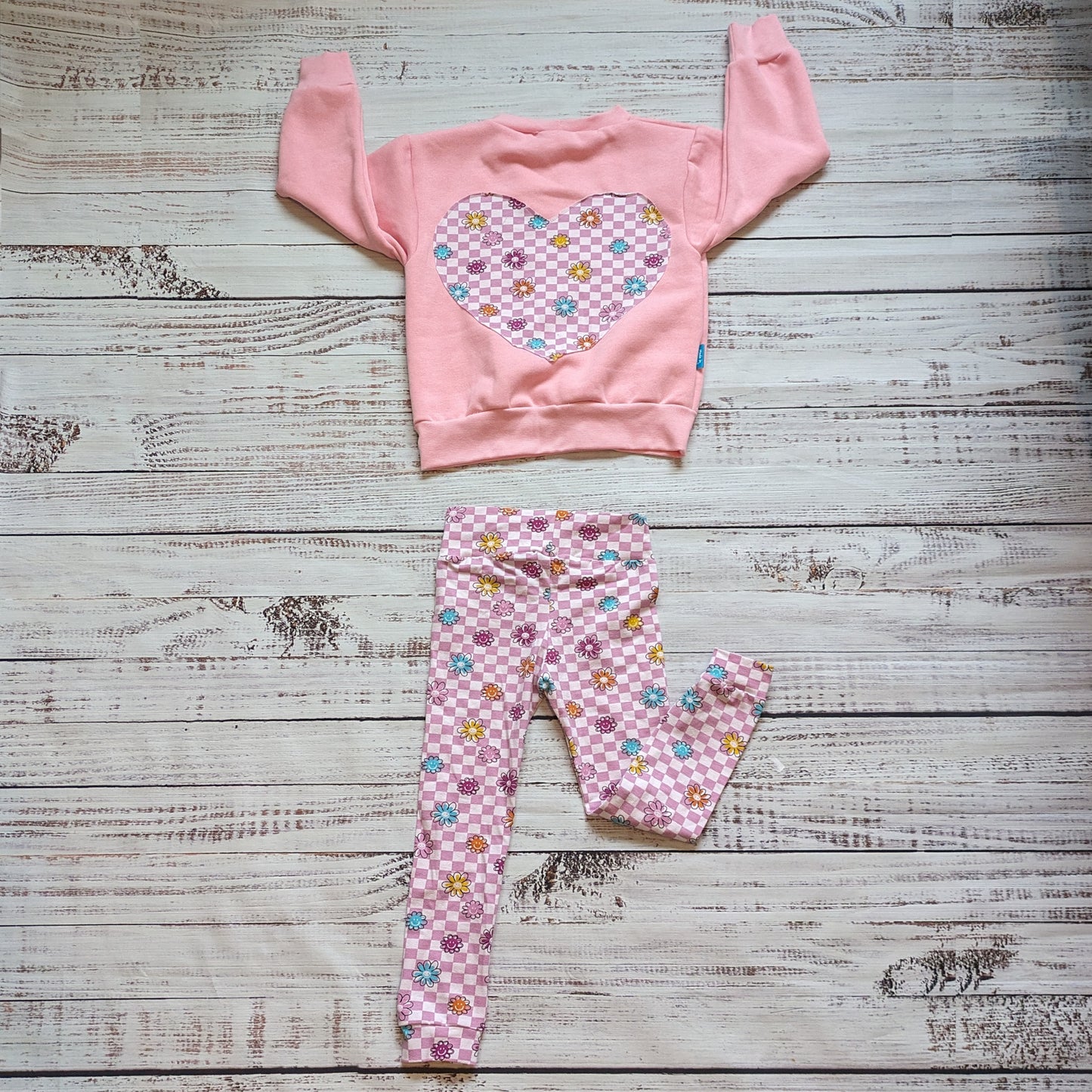 Soft and stretchy kids leggings handmade using pink checked happy flowers cotton jersey. With smiling flowers on a pink checked background. Shown with a matching pink checked happy flowers heart sweatshirt.