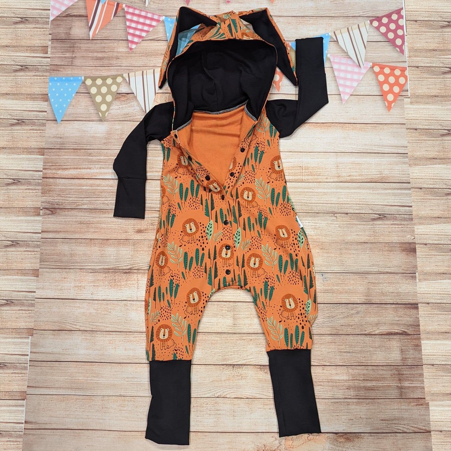 The ferociously fun orange lions bunny romper. Handmade using warm orange lions cotton French terry and black cotton jersey. Featuring front poppers and fun bunny ears on the hood. Shown with some of the poppers open.