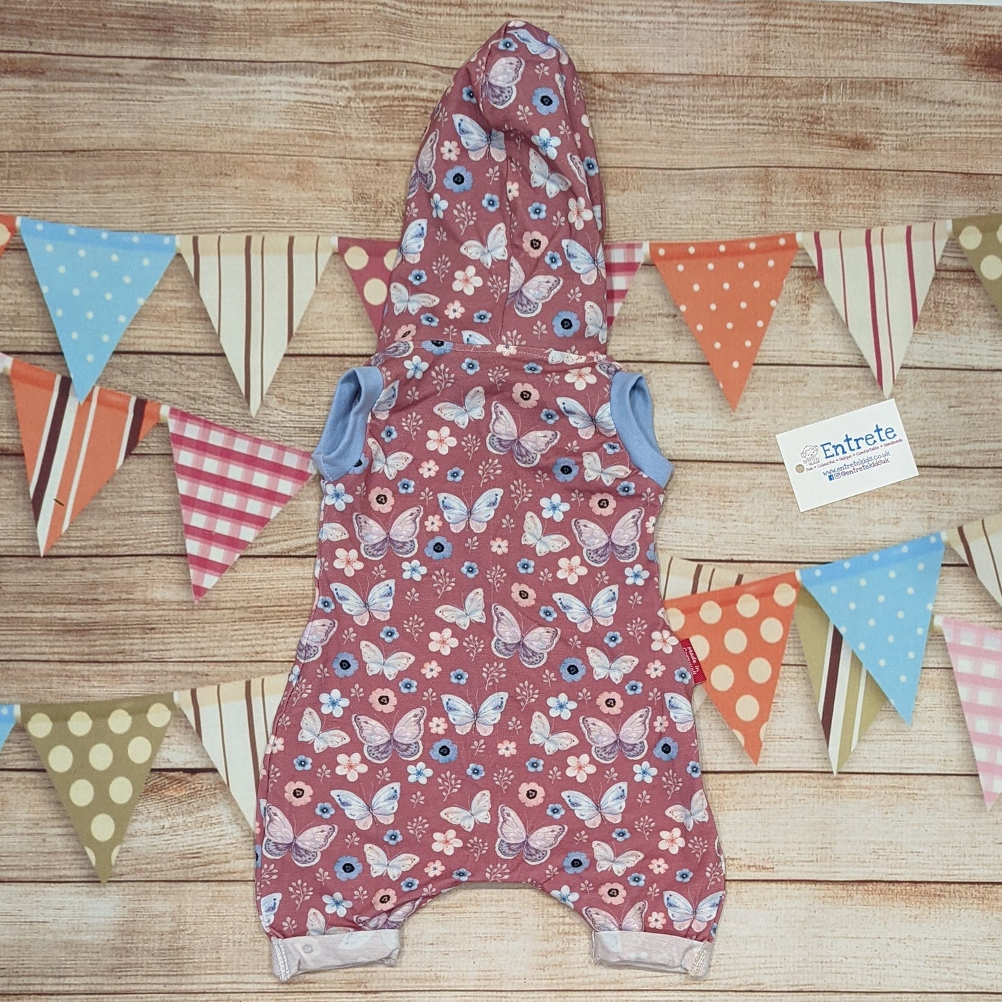 Pretty pink butterflies hooded bummie romper. Handmade using organic pink butterflies cotton jersey, sky blue cotton jersey and sky blue cotton ribbing. Shown from the rear.