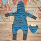 Kids hooded long sleeve romper, handmade using blue surf campervan cotton jersey, contrasting grey cotton jersey cuffs, grey ribbing around the hood and striped hood lining. Shown from the rear with a matching bamboo bib.