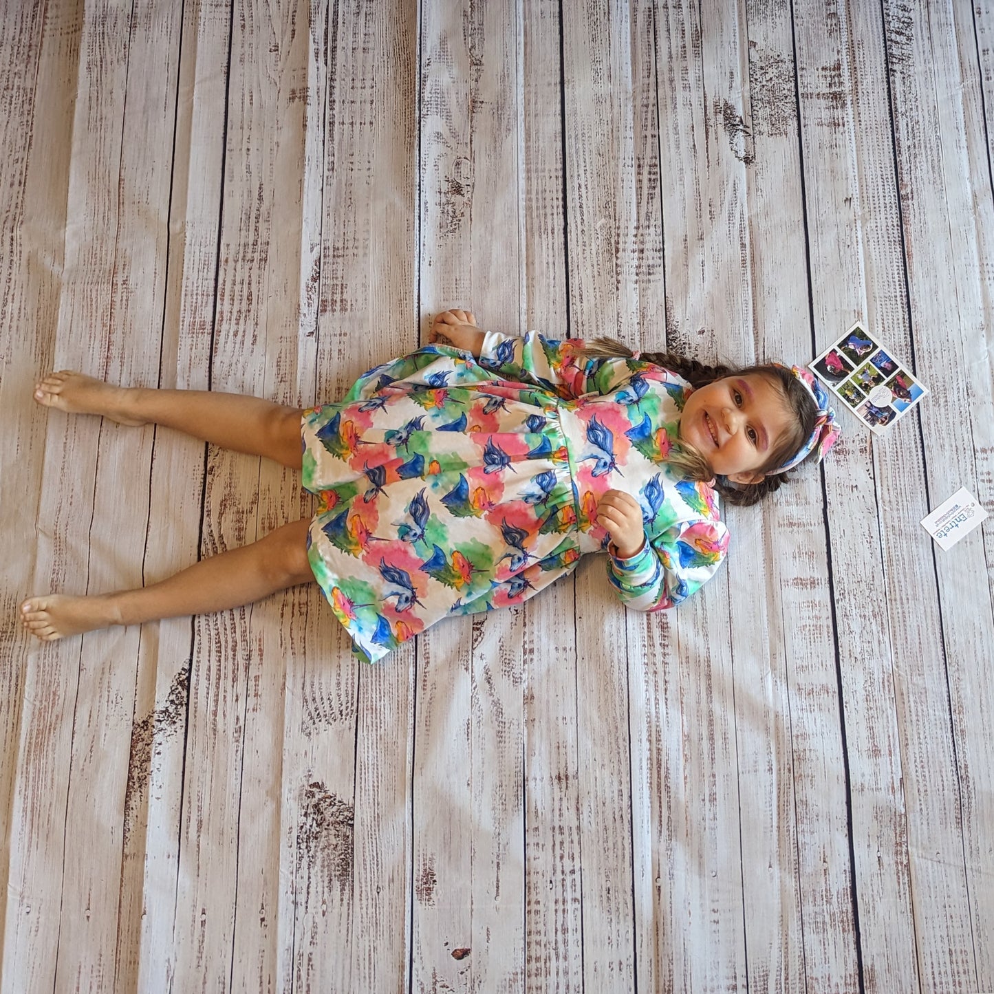 Sophie modelling the long sleeve colourful unicorns on white dress with a matching headband.