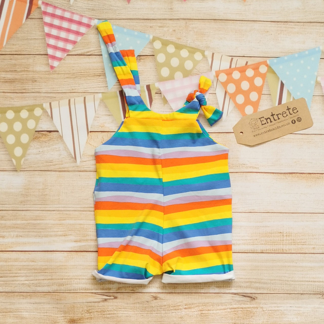 Rear of Unisex Kids Tie Strap Dungaree Shorts, handmade using red rainbow striped cotton jersey and yellow organic cotton jersey. With rolled cuffs and tie shoulder straps that are infinitely adjustable, perfect for growing kids.