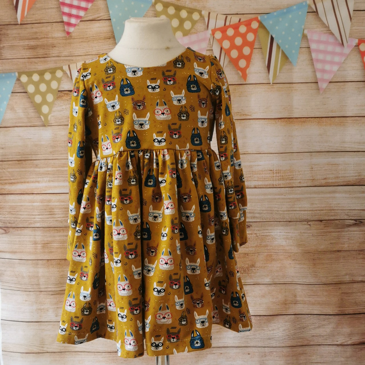 Adorably fun girls and babies back popper dress. Handmade using soft and comfy mustard bunny faces cotton jersey. Shown with long sleeves. on a mannequin.